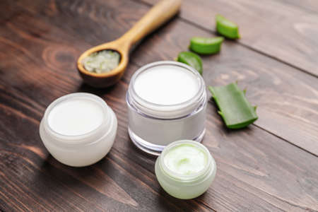 Jars of natural cream and spoon with aloe pieces on wooden backgroundの写真素材