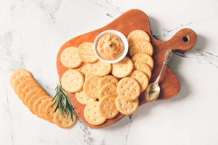 Board with tasty crackers and peanut butter on light backgroundの写真素材