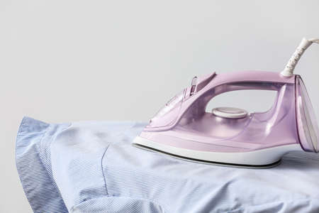 Electric iron with clothes and board on light backgroundの写真素材