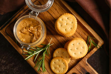 Board with tasty crackers and jar with peanut butter on dark backgroundの写真素材