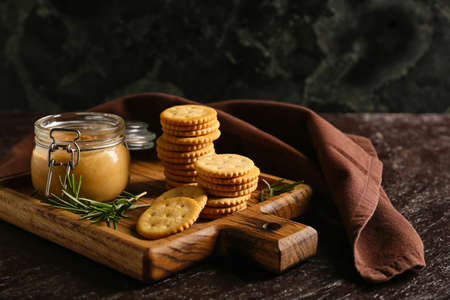 Board with tasty crackers and jar with peanut butter on dark backgroundの写真素材