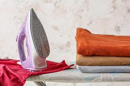 Electric iron and clean clothes on light backgroundの写真素材
