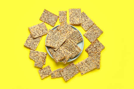 Tasty crackers with seeds in plate on color background