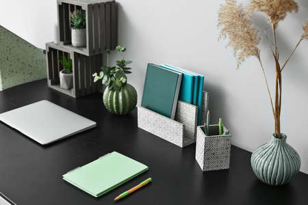 Modern workplace with laptop and organizers near light wall