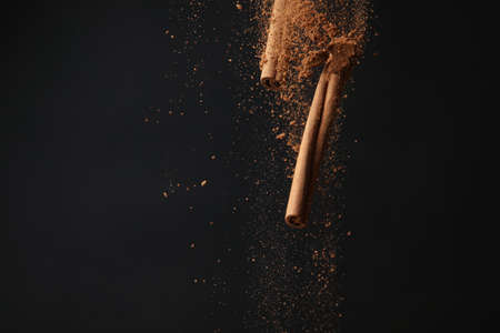 Falling cinnamon sticks and powder on dark backgroundの写真素材