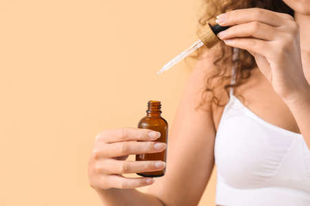 Beautiful African-American woman with essential oil on color background, closeupの写真素材