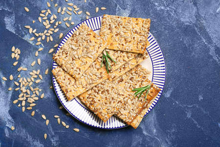 Tasty crackers with seeds in plate on color backgroundの写真素材