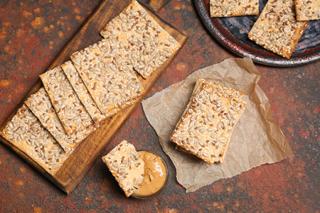 Tasty crackers with seeds and peanut butter on grunge background