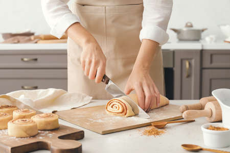 Woman preparing tasty cinnamon rolls in kitchen