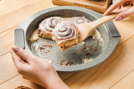 Woman taking tasty cinnamon roll from baking dish on tableの写真素材