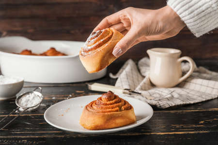 Woman taking tasty cinnamon roll from plate on tableの写真素材