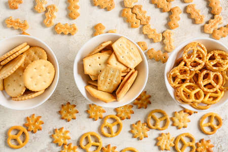 Bowls with tasty different crackers on light background