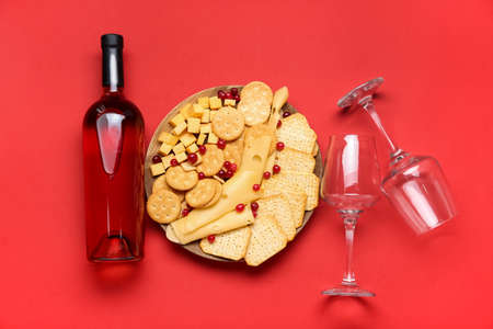 Plate with tasty crackers, cheese and bottle of wine on color backgroundの写真素材