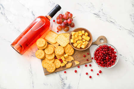 Board with tasty crackers with cheese, bottle of wine and snacks on light backgroundの写真素材