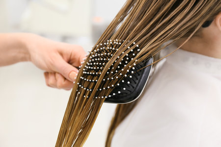 Female hairdresser combing wet hair of client in beauty salon, closeupの写真素材