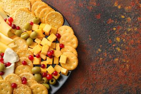 Plate with tasty crackers with cheese and snacks on grunge backgroundの写真素材