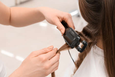 Female hairdresser curling hair of client in beauty salon, closeupの写真素材