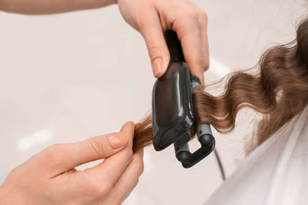 Female hairdresser curling hair of client in beauty salon, closeupの写真素材