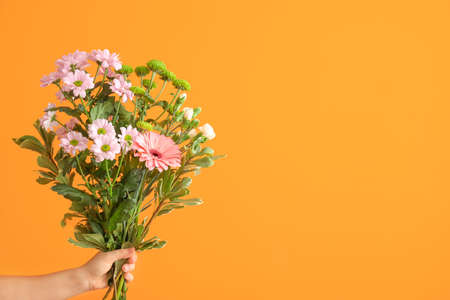Hand with bouquet of beautiful flowers on color backgroundの写真素材