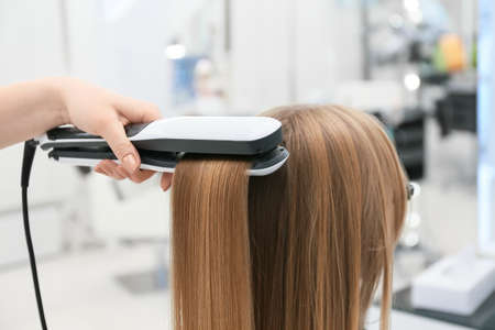 Female hairdresser straightening hair of client in beauty salon, closeupの写真素材