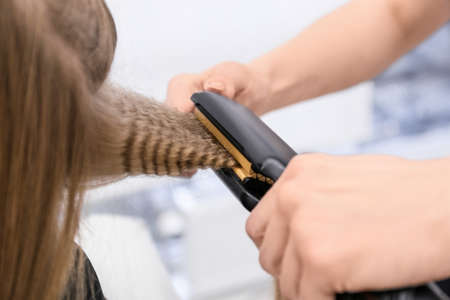 Female hairdresser curling hair of client in beauty salon, closeupの写真素材