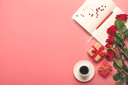 Gifts with rose flowers, notebook and cup of coffee on color backgroundの写真素材
