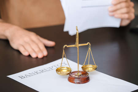 Scales of justice and paper with word BANKRUPTCY on table