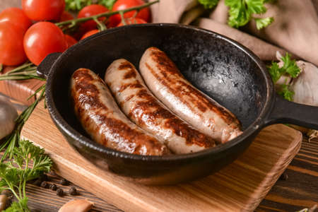 Frying pan with delicious grilled sausages on wooden backgroundの写真素材