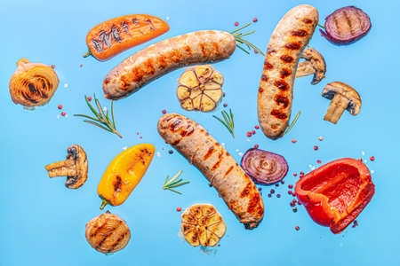Delicious grilled sausages and vegetables on color backgroundの写真素材