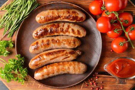 Plate with delicious grilled sausages on wooden backgroundの写真素材