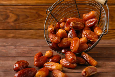 Metal basket with sweet dried dates on wooden background