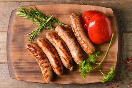 Board with delicious grilled sausages on wooden backgroundの写真素材