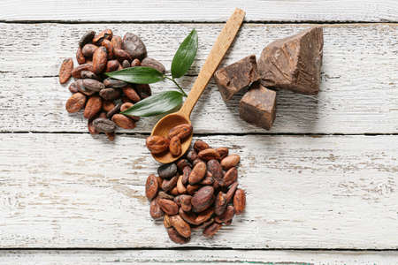 Spoon with cocoa beans and butter on white wooden background