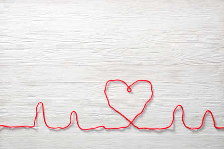 Cardiogram and heart made of thread on white wooden background