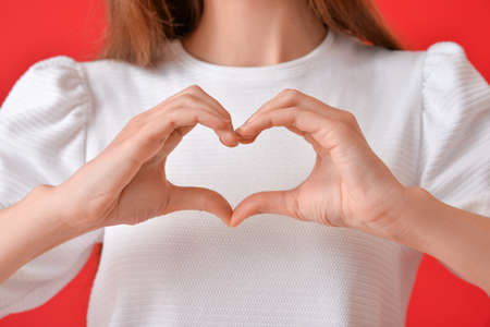 Young woman making heart with her hands on color background, closeupの写真素材