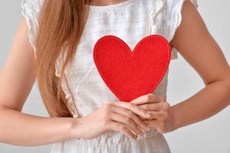 Young woman with red heart on gray background, closeupの写真素材