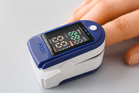 Hand with pulse oximeter on gray background