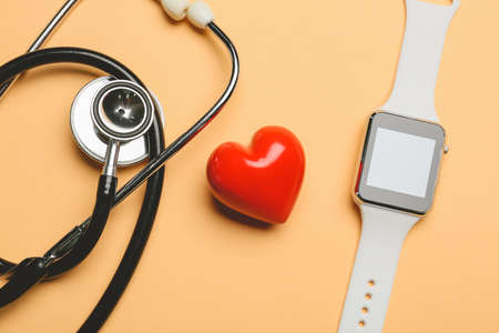 Red heart with fitness band and stethoscope on color background