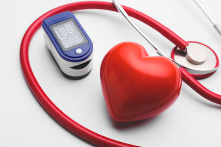 Red heart with pulse oximeter and stethoscope on white backgroundの写真素材