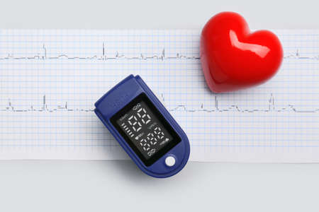 Red heart with pulse oximeter and cardiogram on gray background