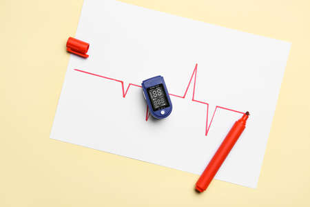 Pulse oximeter and paper sheet with drawn cardiogram on color backgroundの写真素材