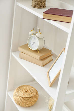 Shelves with alarm clock and decor near white wall