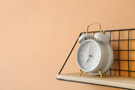 Shelf with alarm clock hanging on color wall