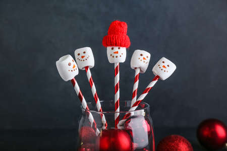 Glass with snowmen made of soft marshmallows and Christmas balls on dark backgroundの写真素材