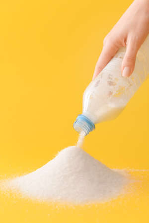 Woman sprinkling sugar from plastic bottle on color backgroundの写真素材