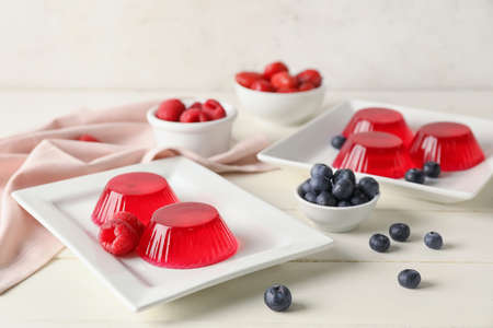 Plates with tasty berry jelly on light background