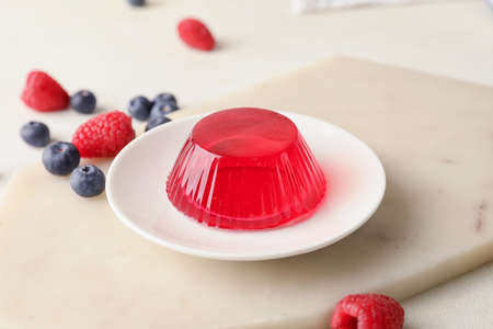 Plate with tasty berry jelly on light background