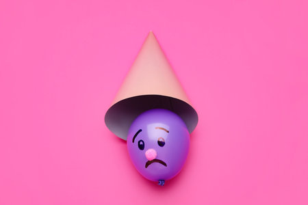 Beautiful balloon with drawn sad face and hat on pink backgroundの写真素材