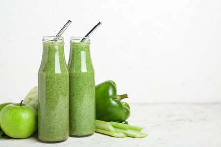 Bottles of healthy green smoothie and vegetables on light backgroundの写真素材
