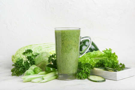 Cup of healthy green smoothie and vegetables on light backgroundの写真素材